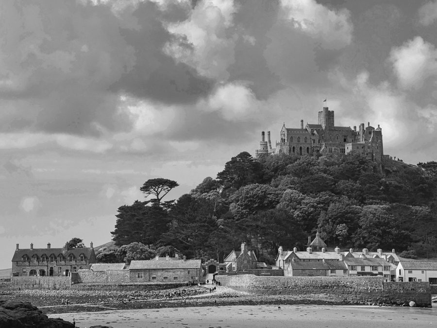 Black-and-white view of a castle on a wooded hill above a small village and shoreline